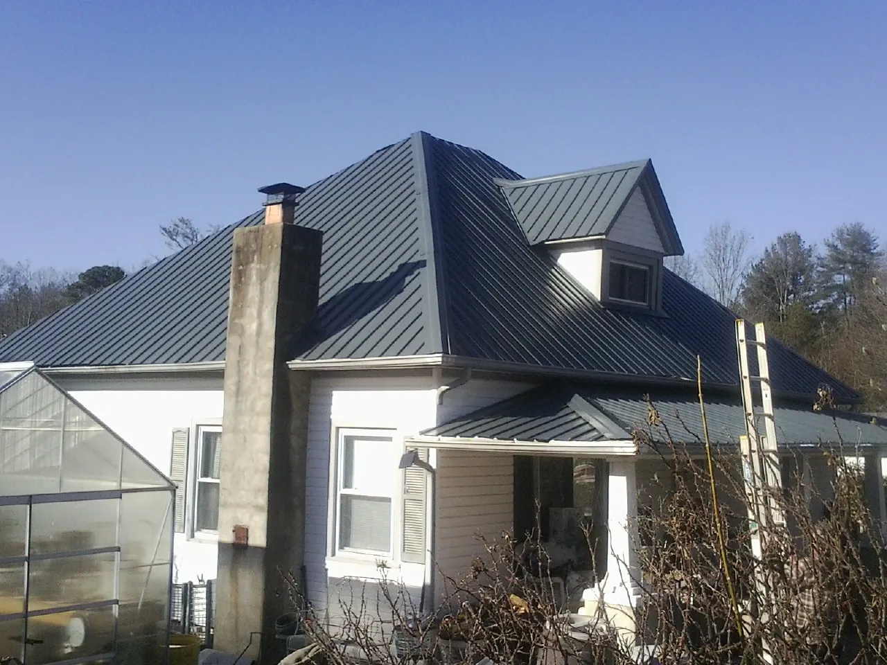 Dark blue standing seam metal roof on a white farmhouse with dormer — Slate & Tile Roof Repair by Roofing Brothers in Schenley
