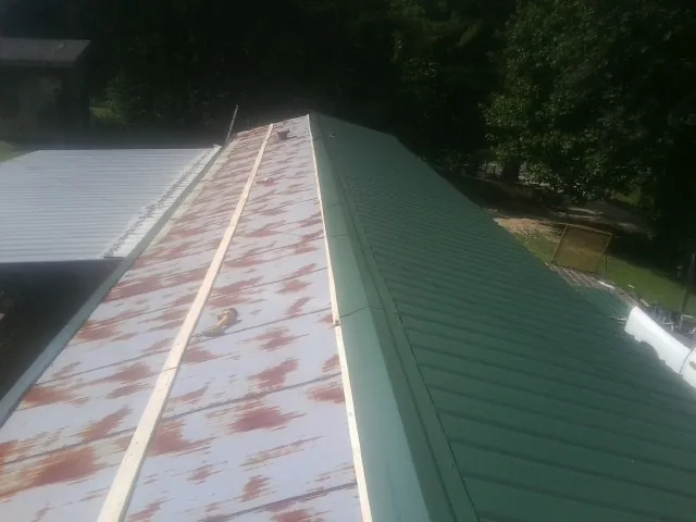 Old rusted panels beside newly installed green metal roofing — Wind Damage Roof Repair by Roofing Brothers in Schenley