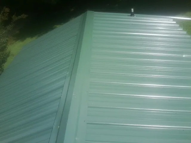 New green metal panels meeting at the ridge of a roof — Flat Roof Repair work by our crew in Schenley