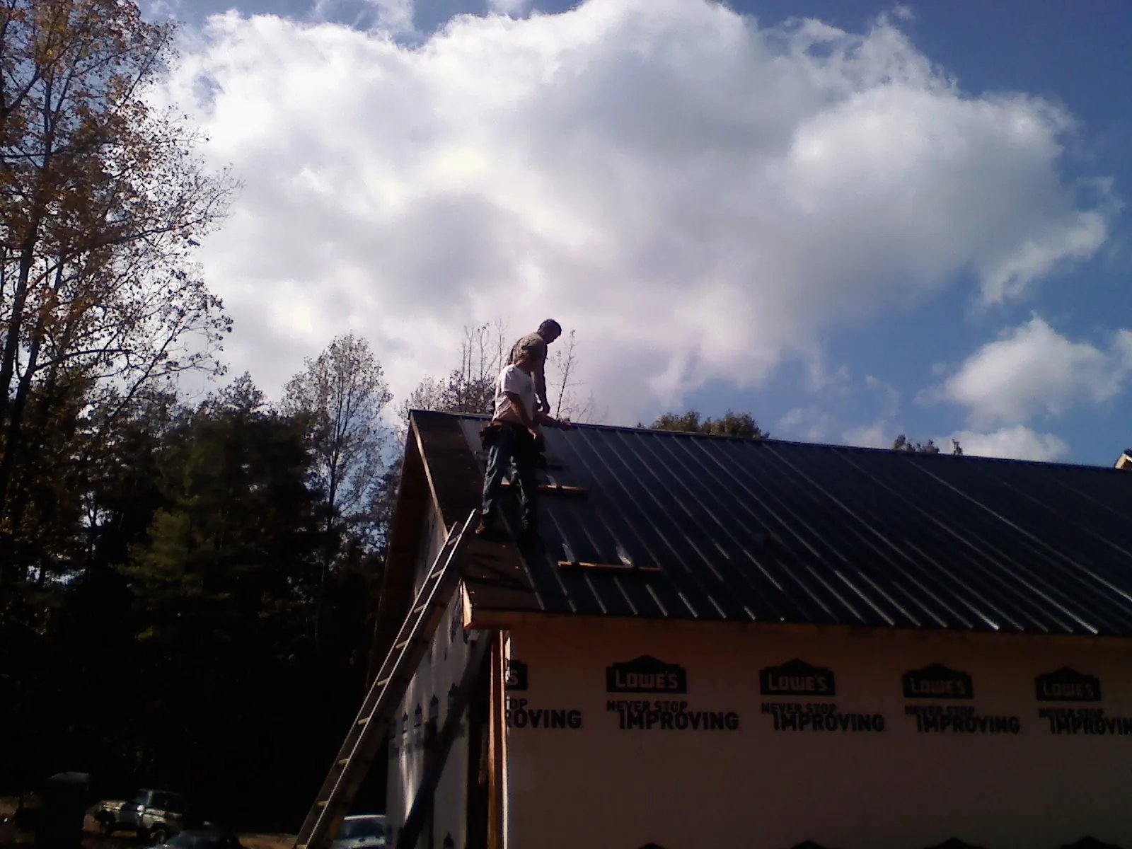 Roofer fastening dark metal panels high against a cloudy sky, from a Roof Inspection job in Schenley