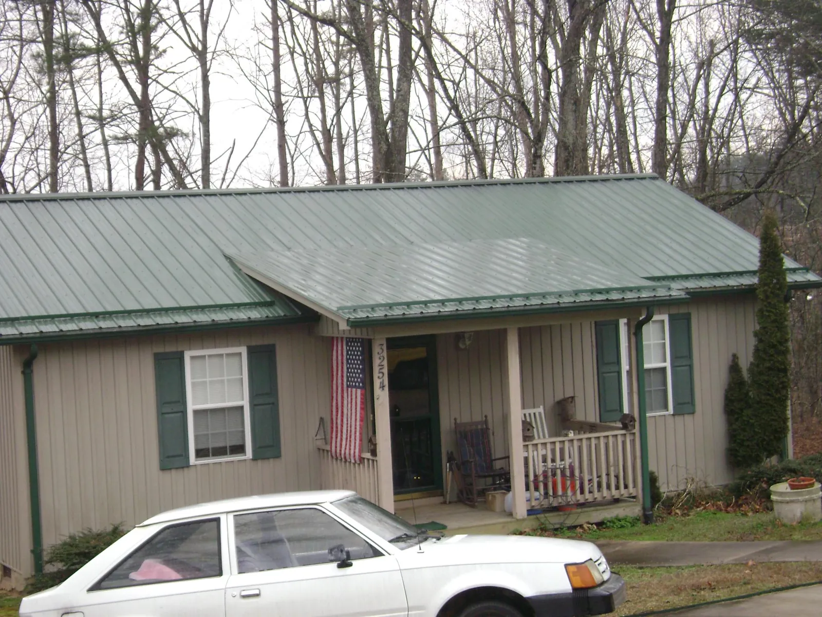 Green metal roof and front porch on a tan sided cottage in Schenley