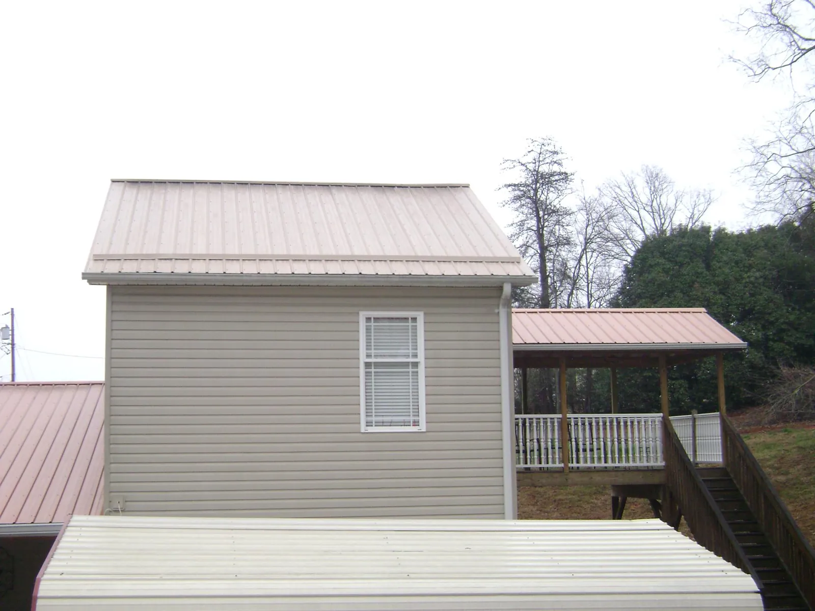 Tan metal roofs on a two story addition and attached porch, from a Roof Replacement job in Schenley